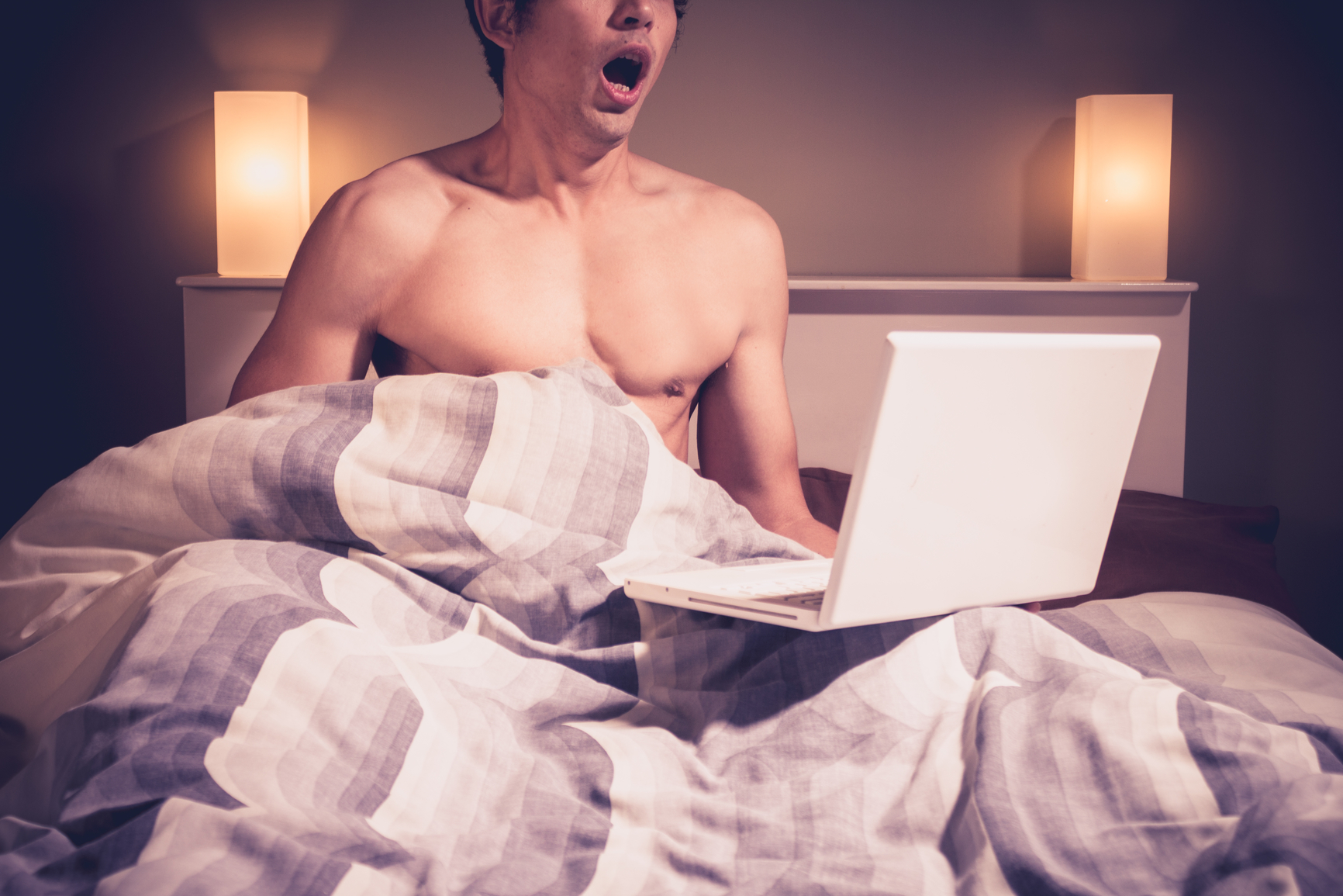 Young man is sitting in bed and watching pornography on laptop 1732 x 1155