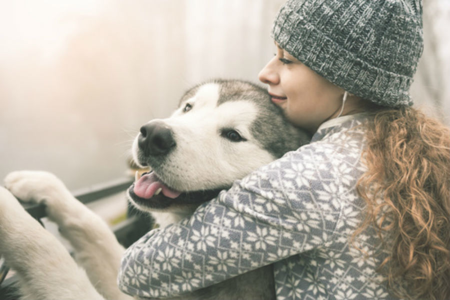 Young woman in sweater hugging her dog 900 x 601