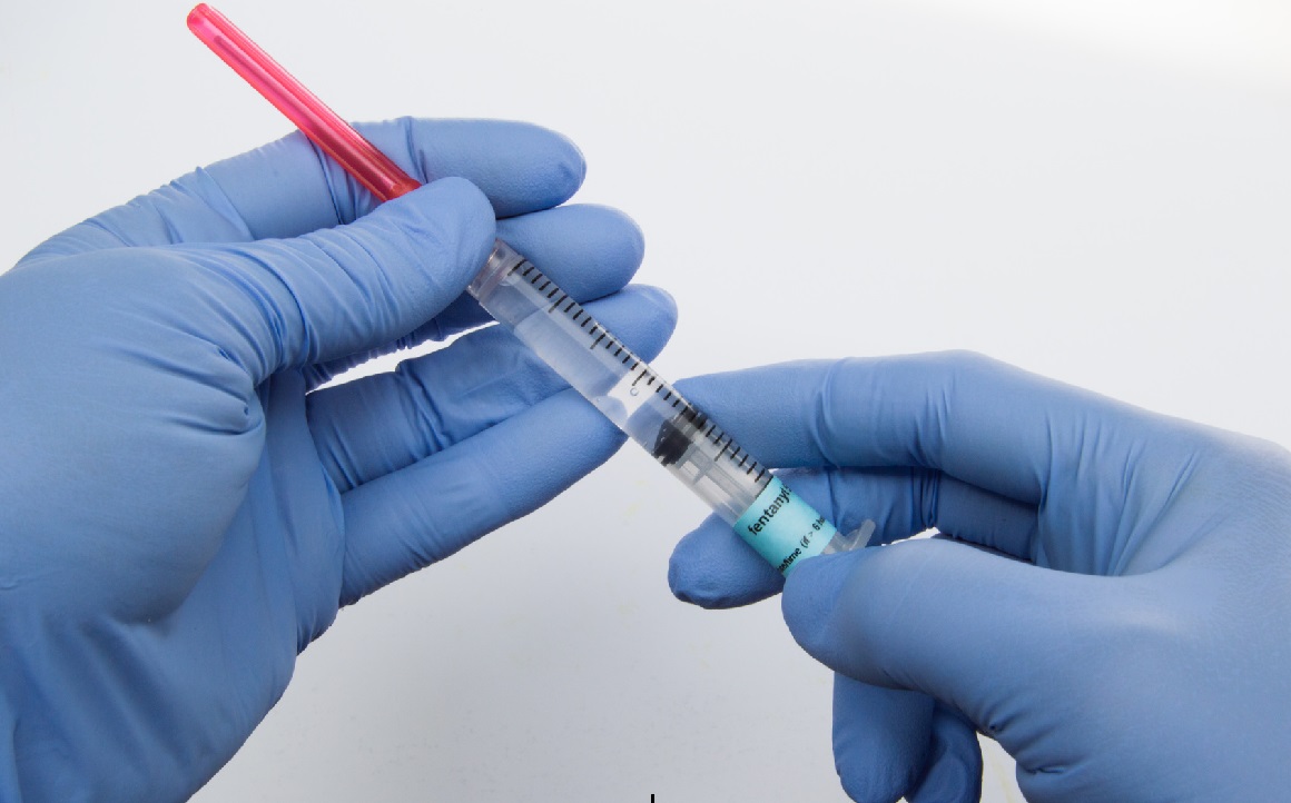 Two Gloved Hands Holding Syringe 1160 x 722