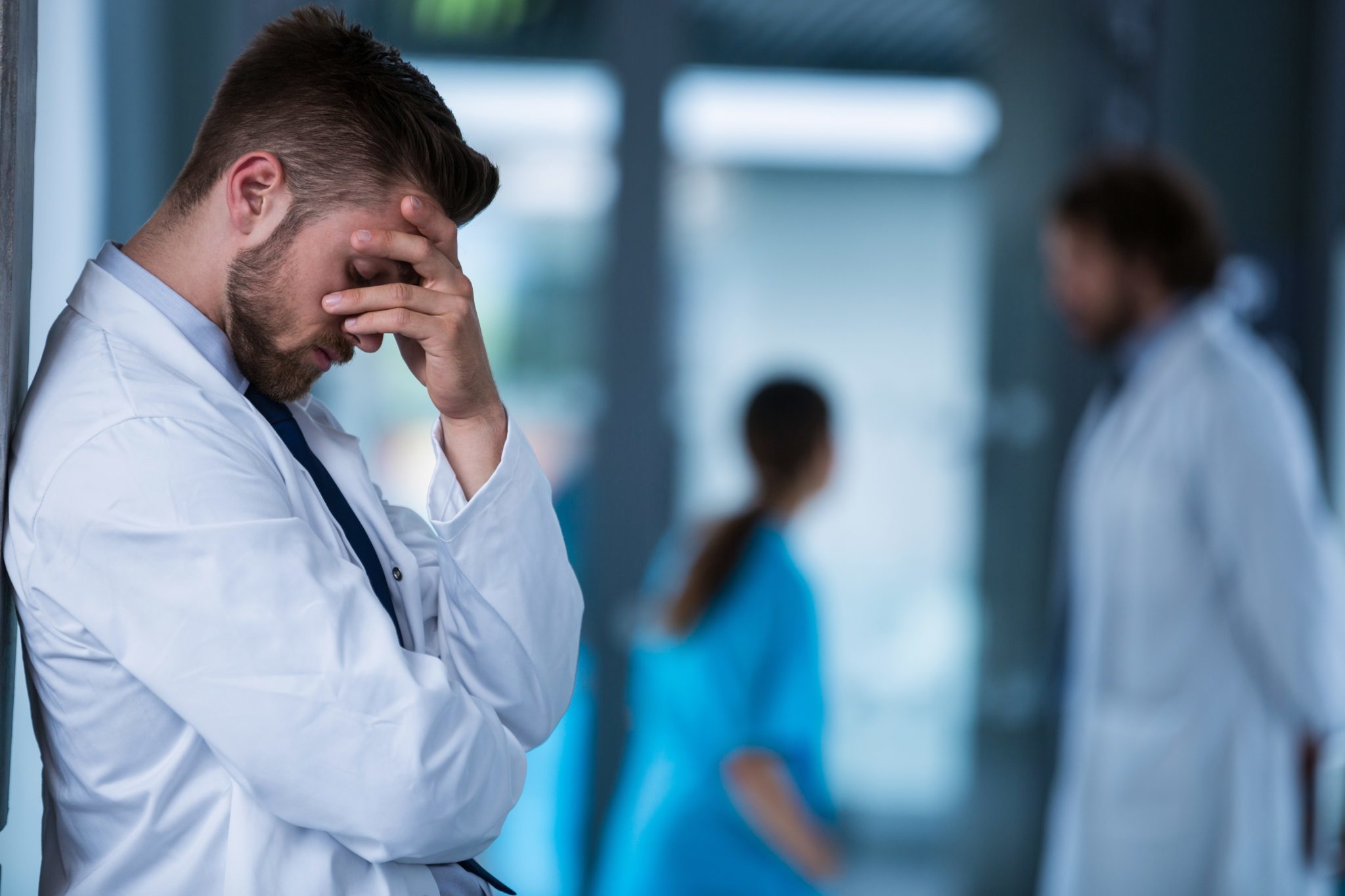 Stressed doctor standing against wall in hospital 2048 x 1365