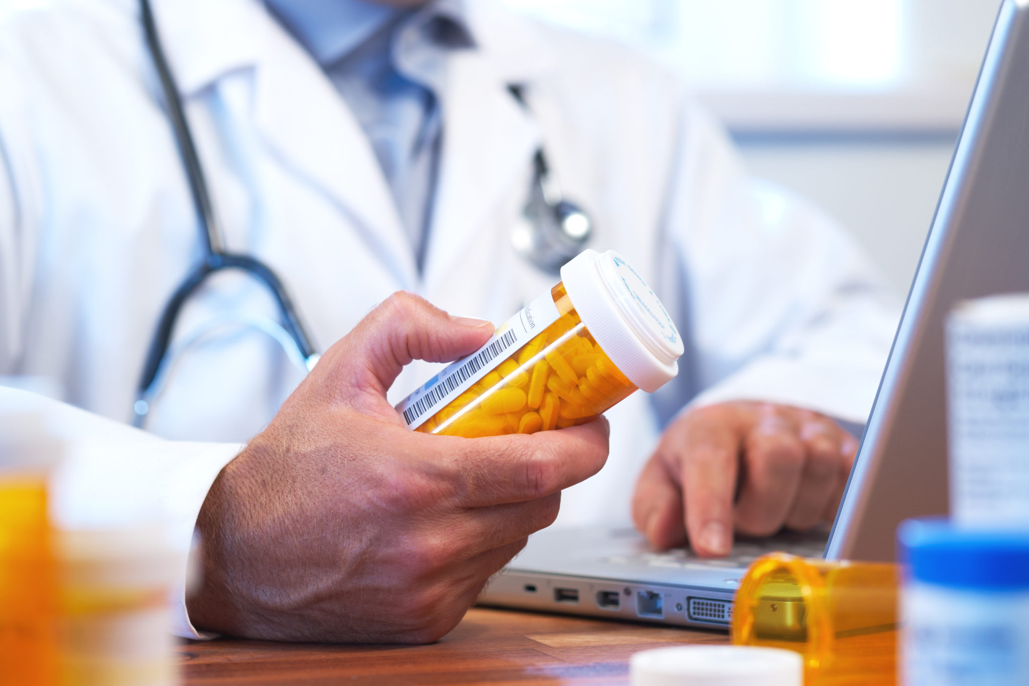doctor holding pill bottle in front of laptop