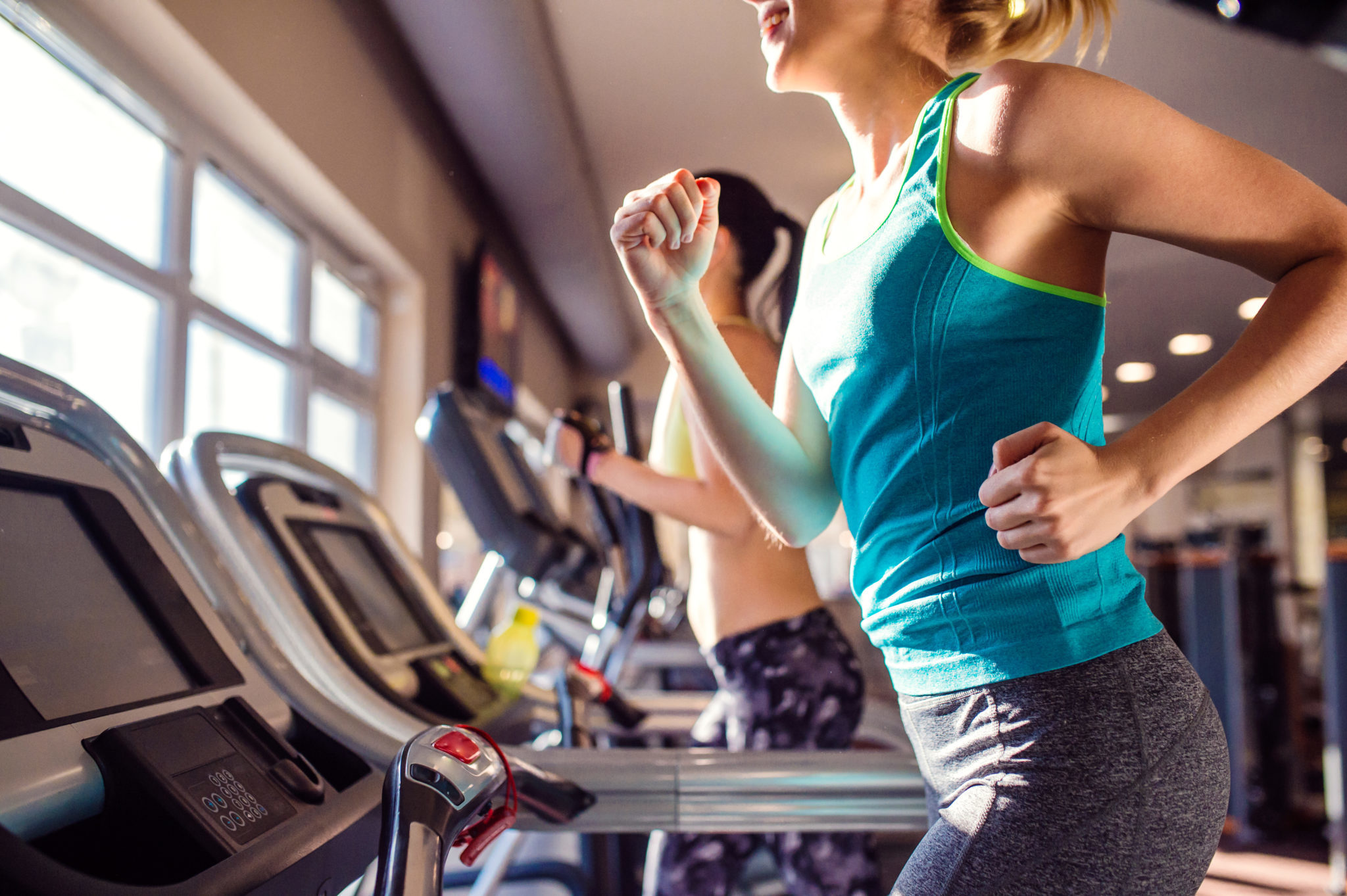 Two attractive fit women running in sports clothes on treadmills in modern gym 2048 x 1363