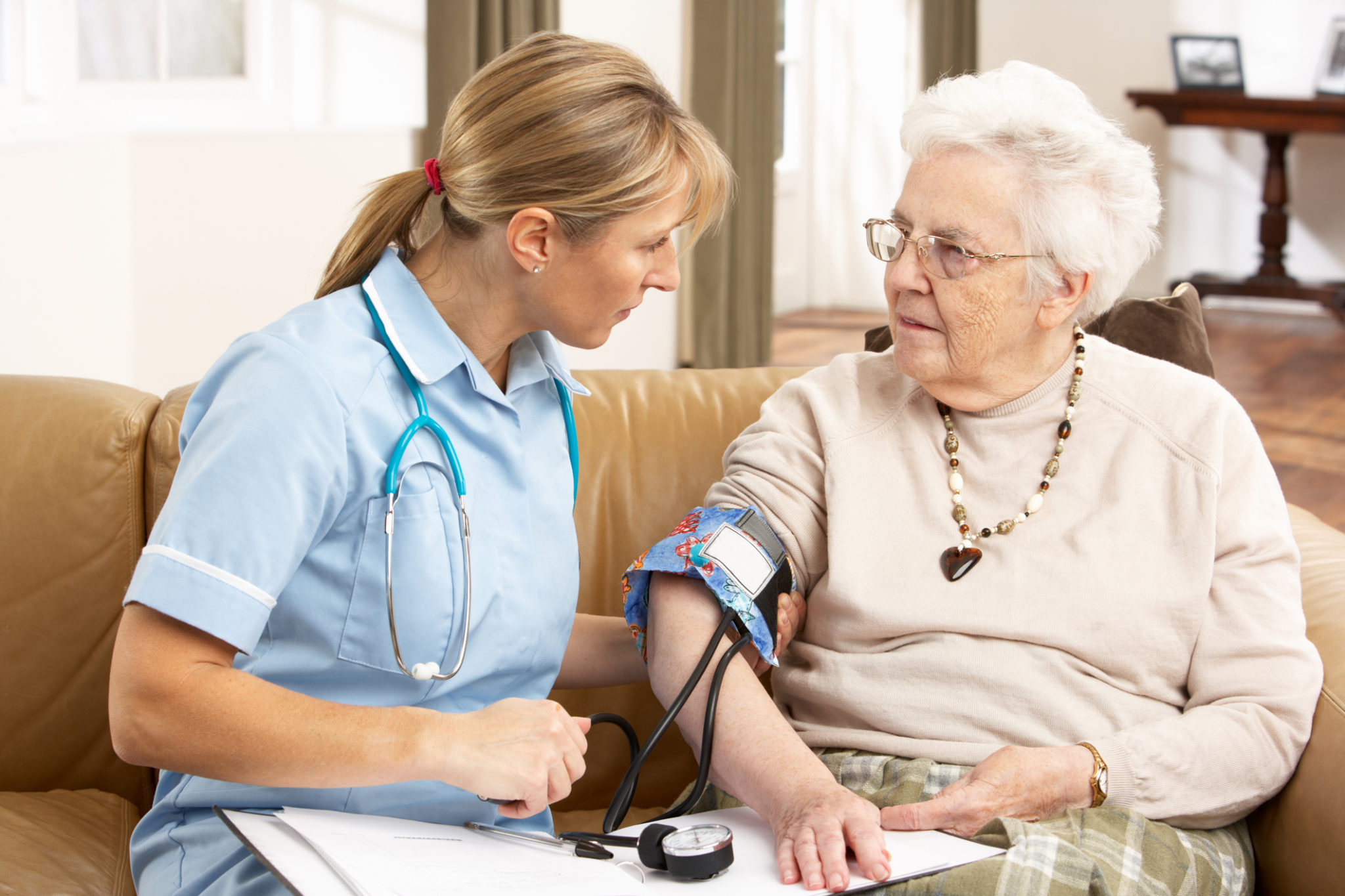 Senior Woman Having Blood Pressure Taken By Health Visitor At Home Looking At Each Other 2048 x 1365