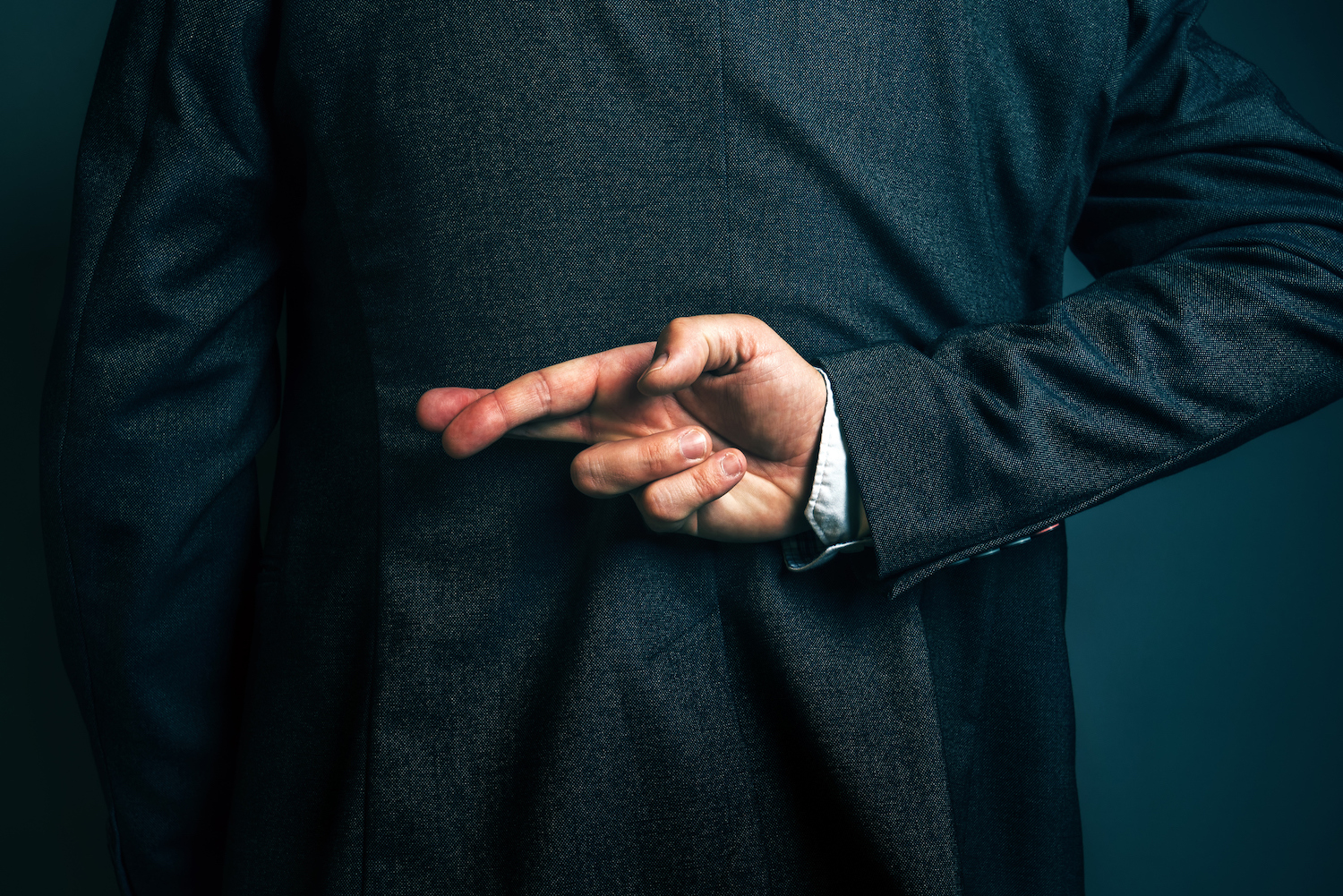 business man in suit with fingers crossed behind his back 1500 x 1001