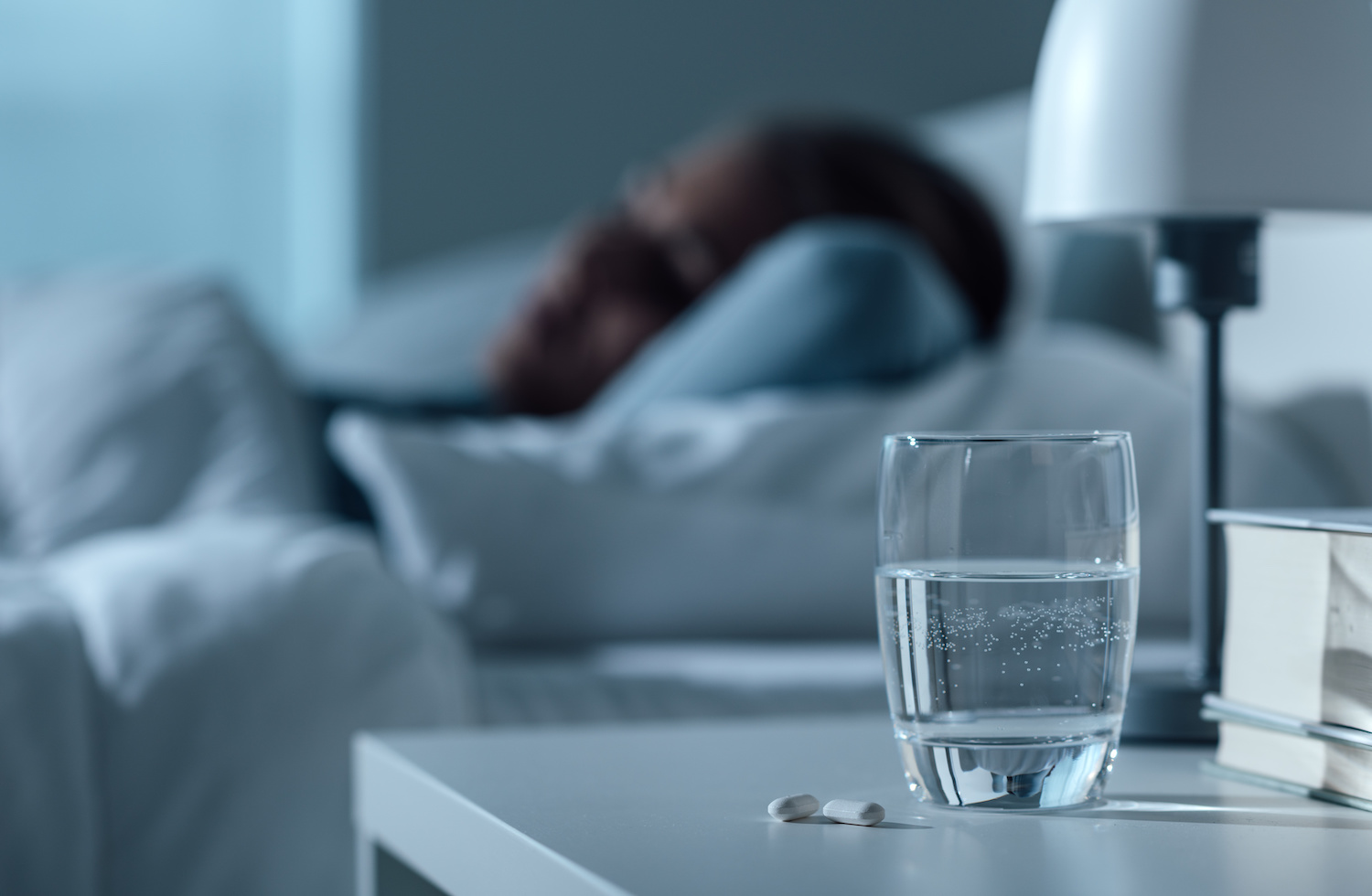 Woman sleeping in her bed at night, glass on water and pills on the foreground, medicine and treatment concept 1500 x 980