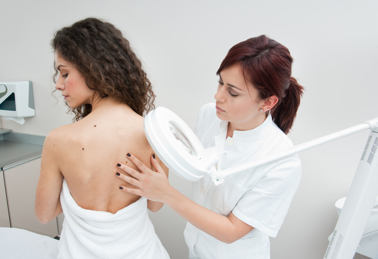 dermatologist doctor inspecting woman skin for moles and melanoma. DepositPhotos 1500x1027