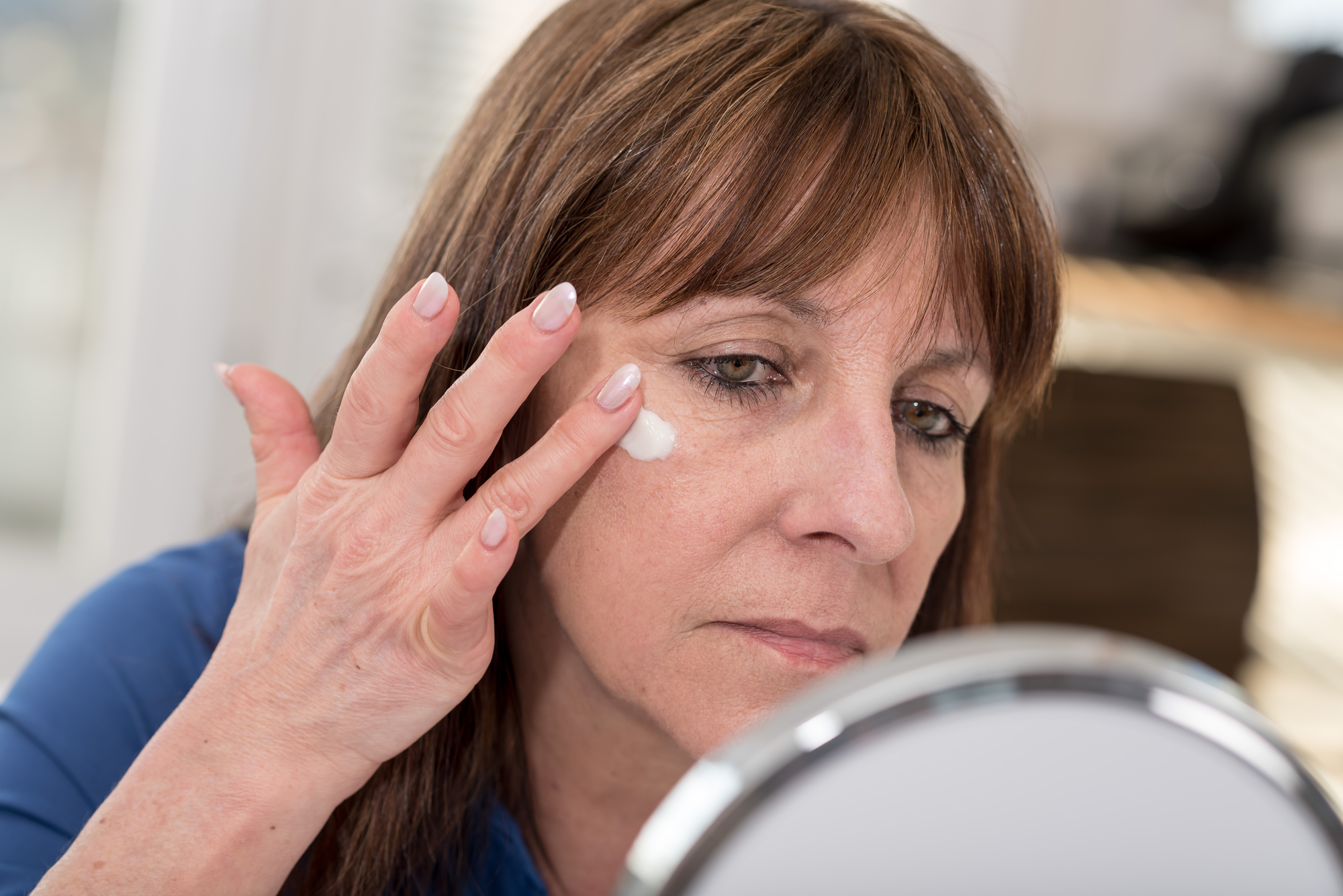 Mature woman putting anti-age cream on her face 2000 x 1335