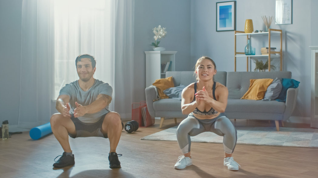 fitness workouts that you can do at home - couple doing squats in the living room
