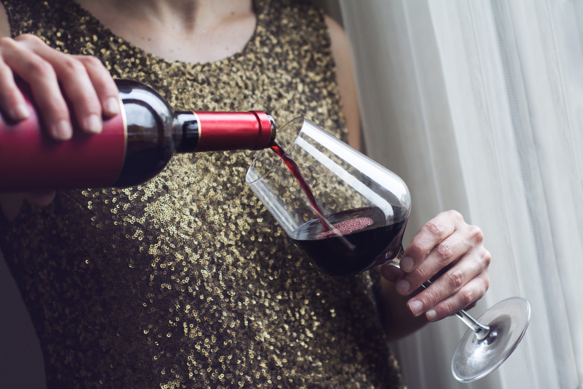 woman with gold spangle dress pouring red wine into glass (2121 x 1414